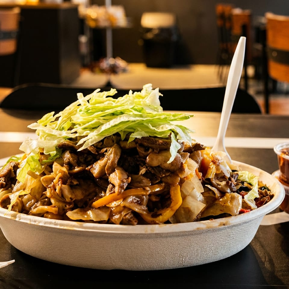 A large bowl of stir-fried noodles with meat, vegetables, and shredded lettuce, with sauce cups.